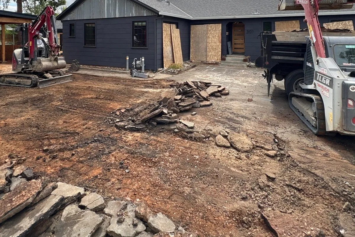 Excavator breaking up an old concrete patio in a backyard