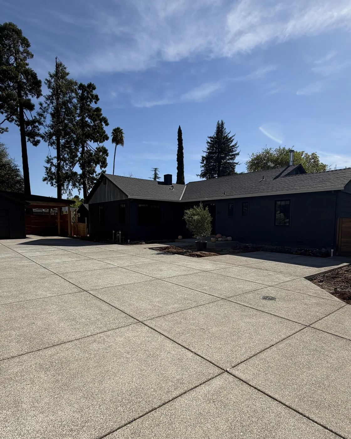 Exposed aggregate concrete driveway and courtyard leading to a dark single story home