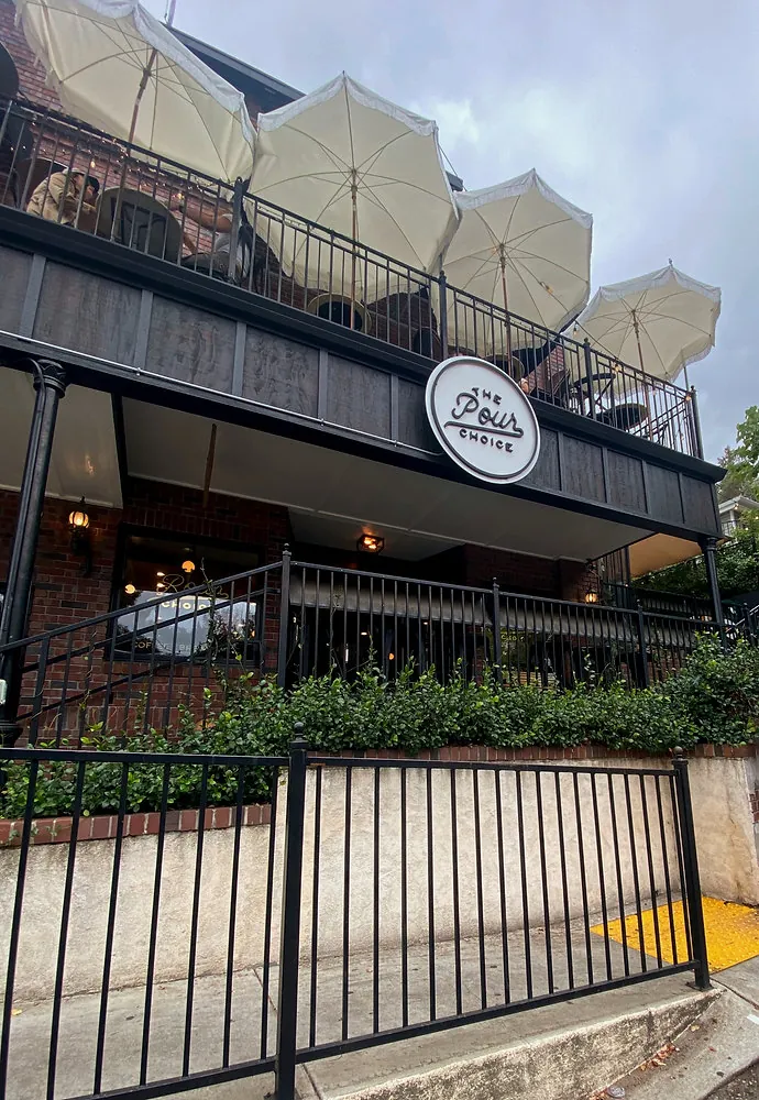 The Pour Choice storefront with its round sign and a rooftop patio lined with white umbrellas