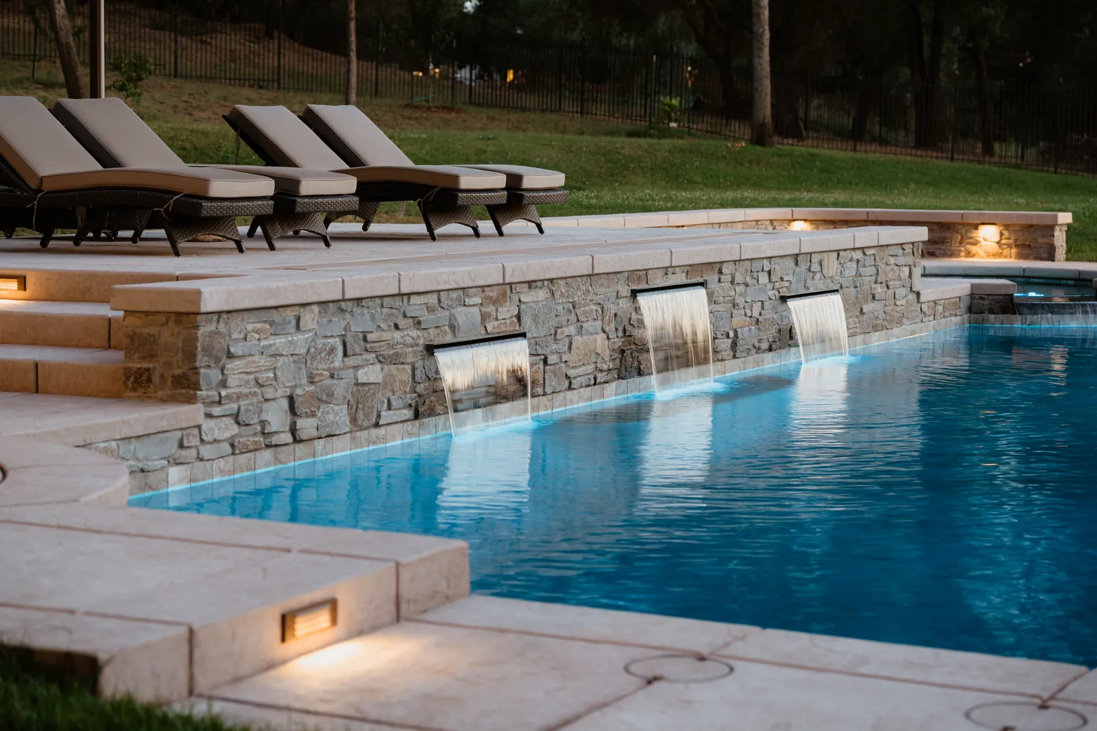 Finished CJR pool with a stacked stone raised wall, sheer descents, and lounge chairs on the deck
