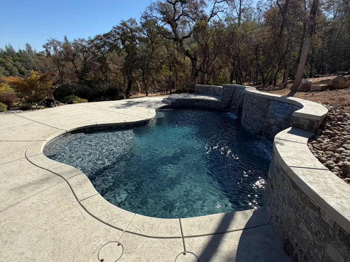 Custom pool with a raised stone wall and stamped concrete deck project by CJR Concrete & Landscape Construction