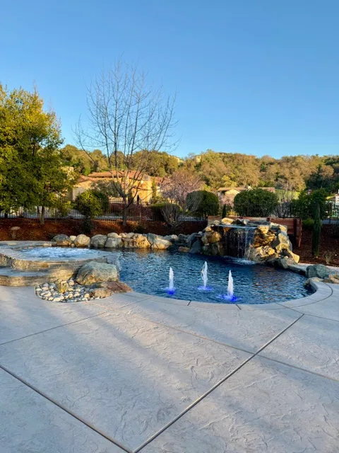 CJR natural rock pool with a waterfall, bubblers, and stamped concrete deck at a Catta Verdera home in Lincoln