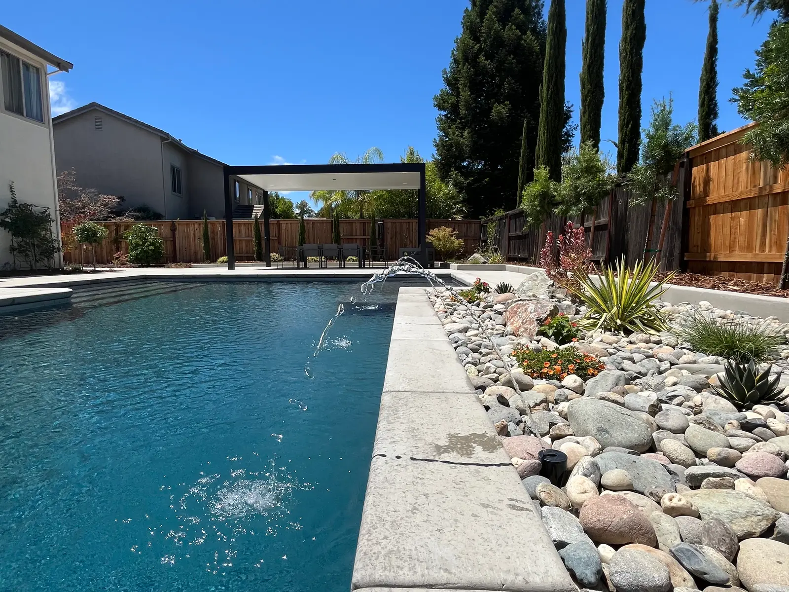Finished CJR backyard with a long pool, smooth concrete decking, river rock, and drought-tolerant planting