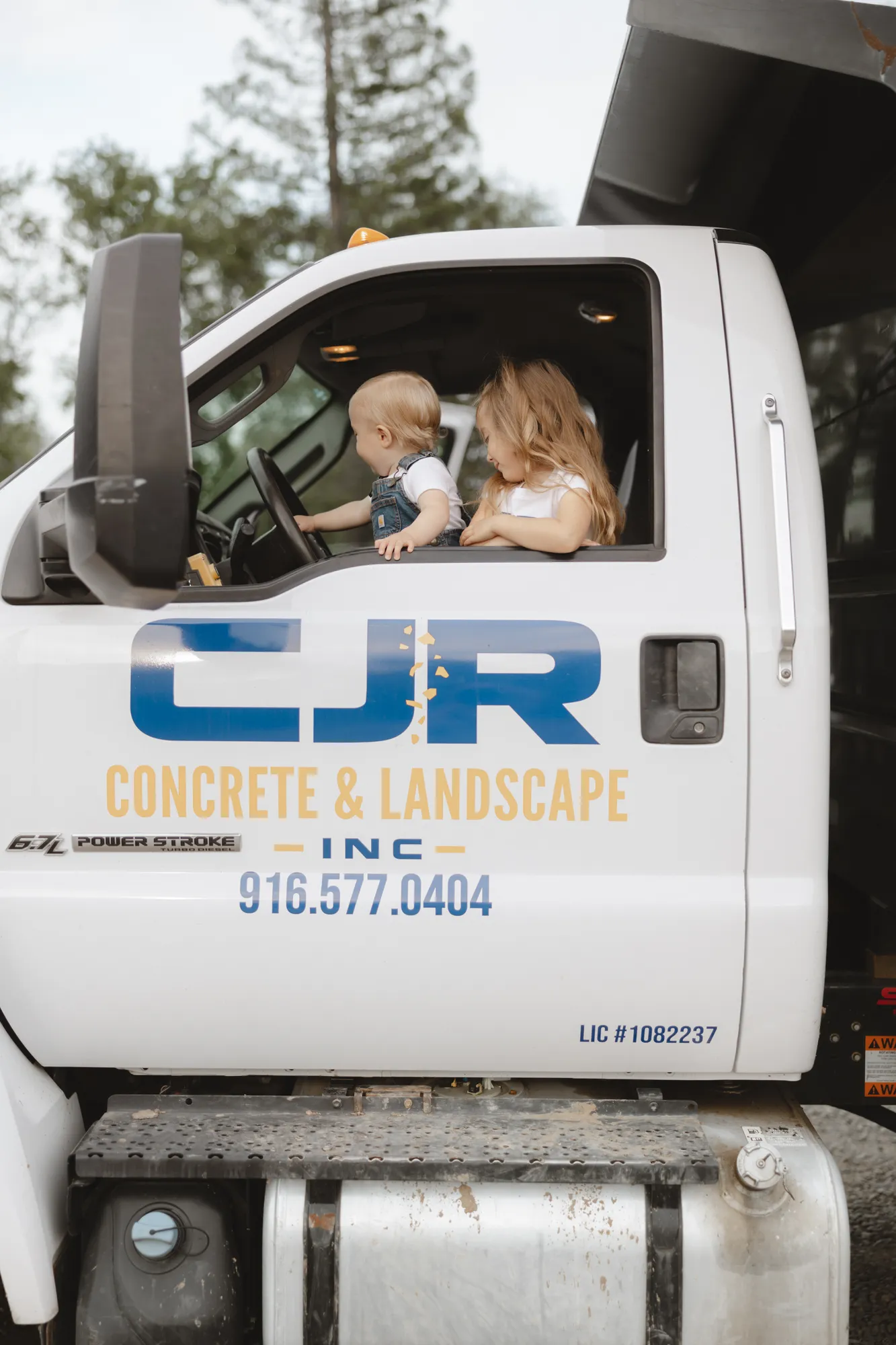 Two young children in the cab of a CJR Concrete & Landscape work truck